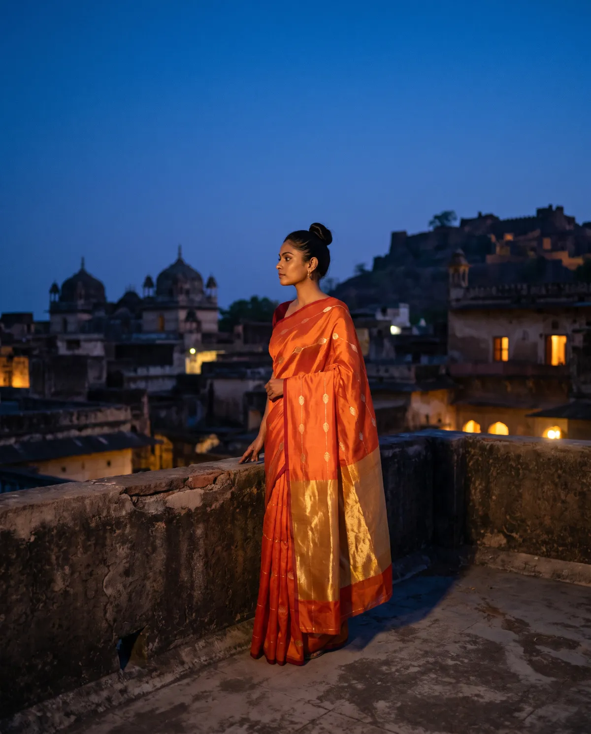A woman in a saffron sari on a rooftop at dusk